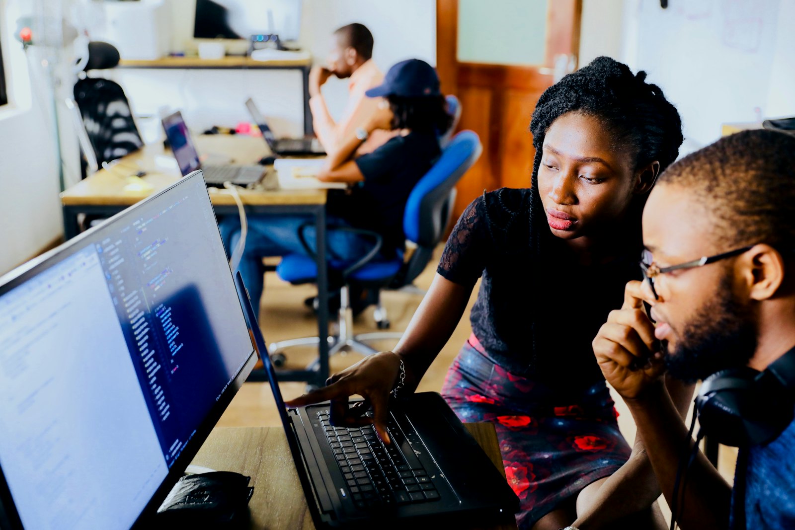 A Black woman and man working together at a computer monitor in an office